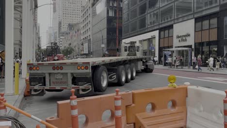 Una-Toma-A-Nivel-De-Calle-De-Un-Camión-Con-Remolque-Sin-Carga,-Retrocediendo-Hacia-Un-Sitio-De-Construcción-En-La-Quinta-Avenida-De-La-Ciudad-De-Nueva-York-En-Un-Día-Soleado.