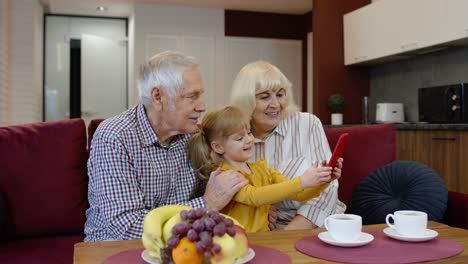 Senior-couple-grandparents-with-child-granddaughter-making-selfie-photos-together-on-mobile-phone