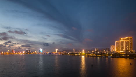 Paisaje-Urbano-De-Da-Nang,-Hora-Azul-Con-Nubes-Dinámicas-Sobre-La-Orilla-Del-Agua-Y-Luces-Brillantes-De-La-Ciudad,-Vietnam