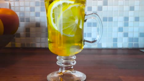 Slow-motion-close-up-footage-of-a-lemon-tea-on-a-kitchen-table-that-features-vibrant-colors-and-oranges-in-the-background