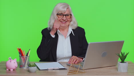 Senior-business-woman-raises-thumbs-up,-agrees,-approve,-likes-good-news-using-laptop,-green-office