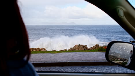 Blick-Aus-Der-Ersten-Person-Aus-Dem-Beifahrerfenster-An-Einem-Stürmischen-Tag,-Als-Die-Welle-über-Den-Felsen-Bricht