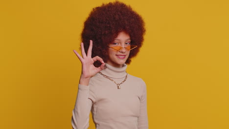 Young-funny-school-girl-in-glasses-looking-approvingly-at-camera-showing-okey-gesture,-like-sign