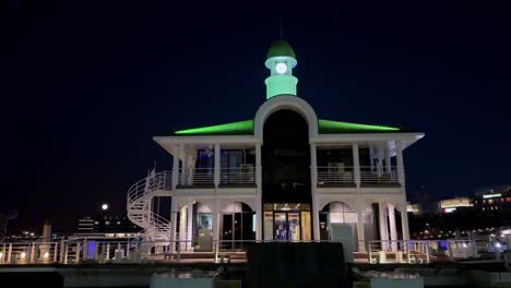 Illuminated-waterfront-building-with-green-lights-at-night