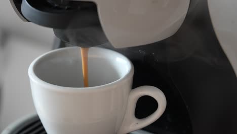 Eine-Nahaufnahme-Einer-Kaffeemaschine,-Die-Frischen-Kaffee-In-Eine-Weiße-Keramiktasse-Gießt-Und-Die-Reichhaltige,-Braune-Flüssigkeit-Einfängt,-Während-Sie-Gleichmäßig-Fließt