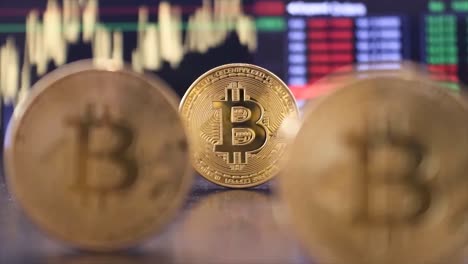 El-Metraje-Que-Cambia-De-Enfoque-Lentamente-Muestra-Tres-Monedas-De-Bitcoin-Y-Finalmente-Llega-Al-Fondo,-Que-Muestra-Gráficos-Y-Tablas-De-Acciones-Y-Criptomonedas-En-Resolución-4k.