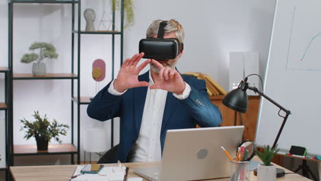 Mature-business-man-in-VR-goggles-watch-virtual-reality-video,-working-on-simulation-game-at-office