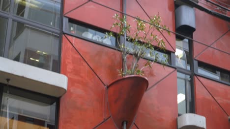 Tilt-up-shot-of-a-potted-plant-attached-to-the-wall-of-an-organic-building-in-Osaka-Namba,-captured-from-below