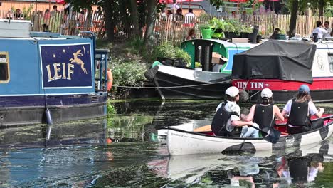 Three-people-rowing-past-No90-Hackney-Wick,-London,-United-Kingdom