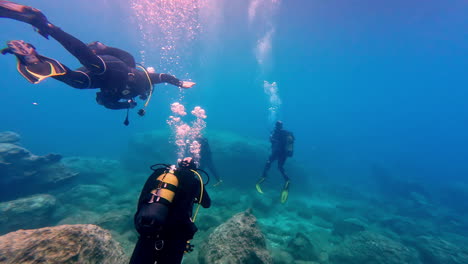 Scuba-divers-exploring-a-rocky-underwater-landscape-in-clear-blue-water