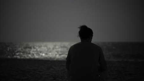 El-Hombre-Se-Sienta-Solo-En-La-Playa-Por-La-Noche,-Usa-Un-Teléfono-Móvil-A-La-Luz-De-La-Luna,-Reflejo-Del-Océano,-Paisaje-Panorámico,-Golfo-Pérsico,-Soledad,-Horizonte,-Olas,-Paz,-Silencio,-Oscuridad,-Paisaje,-Medianoche,-Costa,-Conexión