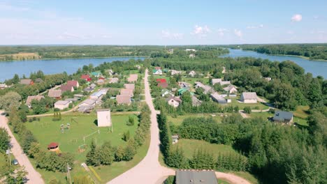 Vista-Aérea-Del-Pueblo-Báltico-Demene,-Ubicado-En-La-Región-De-Latgola,-Que-Muestra-El-Diseño-De-Calles,-Casas-Y-Un-Pintoresco-Lago.