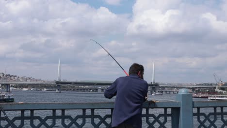 A-fisherman-pulls-strings-from-his-rod-with-the-Galata-Bridge-in-the-backdrop,-Istanbul,-Turkey