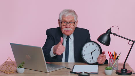 Senior-smiling-businessman-showing-time-on-wall-office-clock,-ok,-thumb-up,-good-approve-success