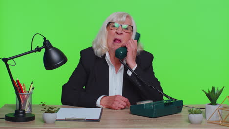 Crazy-senior-businesswoman-talking-on-wired-vintage-telephone-fooling-making-silly-humor-comic-faces