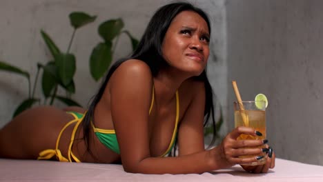 Asian-bikini-model-in-a-yellow-and-green-bikini-relaxes-on-a-sunbed,-enjoys-a-refreshing-tropical-cocktail