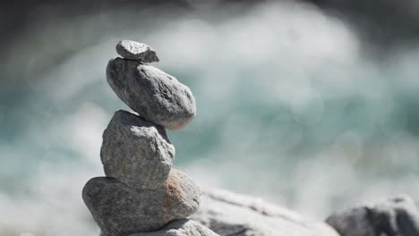 Neatly-stacked-rocks-on-a-riverbank,-with-a-flowing-river-in-the-background