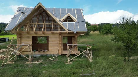 Casa-De-Madera-En-Construcción,-Hecha-De-Troncos-Y-Ubicada-En-Un-Hermoso-Paisaje-Rodeado-De-Exuberante-Vegetación,-Césped-Y-árboles-Bajo-Un-Cielo-Azul.