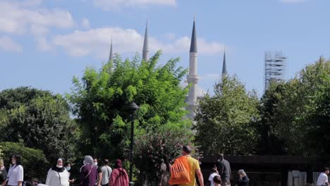 People-traverse-a-pedestrian-area-in-Istanbul,-Turkey,-with-the-towers-of-a-mosque-in-the-backdrop