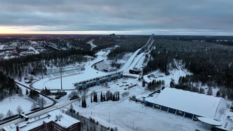 Panoramic-drone-shot-circling-the-Salpausselka-sports-complex,-winter-sunset-in-Lahti,-Finland