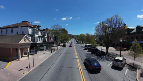 Aerial-tracking-shot-of-car-on-main-road-of-american-historic-town-with-storefronts