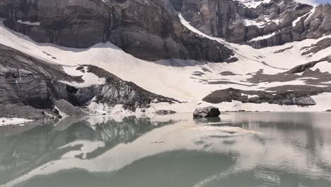 Serene-glacial-lake-with-surrounding-snow-covered-mountains-in-Klausenpass,-Urner-Boden,-Switzerland