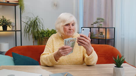 Mujer-Mayor-Sonriente-Y-Feliz-Contando-Dinero-En-Efectivo-Usando-El-Teléfono-Inteligente-Para-Ganar-Lotería