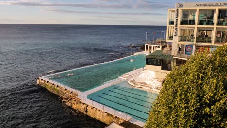 Weite,-Erhöhte-Sicht-Auf-Bondi-Eisberge-Mit-Menschen,-Die-Bei-Sonnenaufgang-Schwimmen