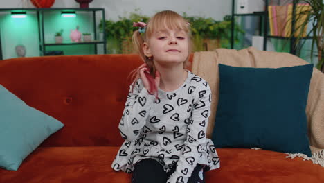 Cheerful-lovely-caucasian-little-toddler-kid-girl-smiling,-looking-at-camera-sitting-on-sofa-at-home