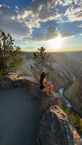 Vertical-View,-Young-Woman-Sitting-on-Lookout-of-Grand-Canyon-of-Yellowstone-National-Park,-Wyoming-USA