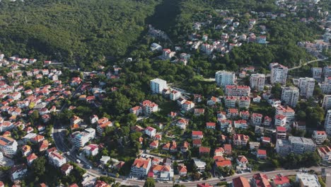 Drone-shot-of-Herceg-Novi,-Monte-Negro,-showcasing-a-charming-village-with-terracotta-roofed-houses,-winding-streets,-lush-greenery,-and-the-Adriatic-Sea-in-the-background