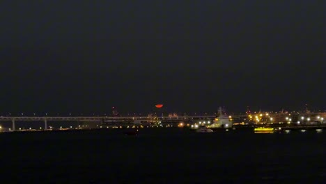 Eine-Brücke-Und-Eine-Stadtlandschaft,-Die-Nachts-Beleuchtet-Sind,-Mit-Einem-Roten-Mond,-Der-Im-Hintergrund-Aufgeht