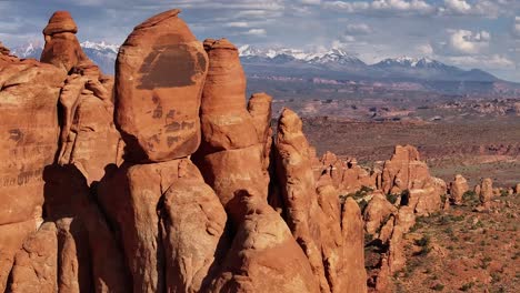 Aerial-americana-view-of-red-rock-formations-with-snow-capped-mountains-backdrop,-Moab-Utah