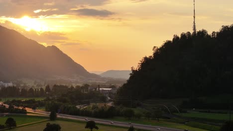 Sunset-view-of-Glarus-Nord,-Switzerland,-featuring-a-TV-tower-on-a-hill-and-a-road-with-car-traffic-in-the-valley