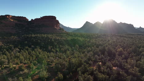 Sun-Rising-Over-Red-Rock-Mountains-With-Green-Forest-In-Sedona,-Arizona,-Aerial-View