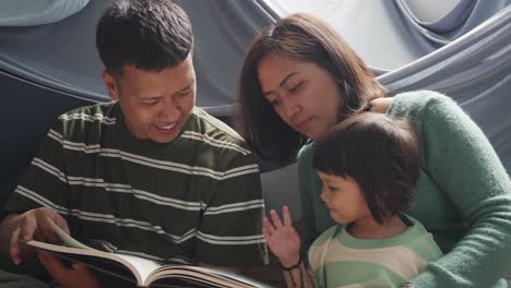 Young-Asian-Father,-Mother-And-Happy-Child-Reading-Books-In-A-Tent-Together-At-Home