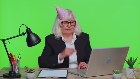 Sad-upset-lonely-senior-businesswoman-celebrating-birthday-party-alone,-holds-cake-at-green-office