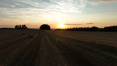 Eine-Beruhigende-Drohnenaufnahme-Eines-Abgeernteten-Feldes-Voller-Heuballen-Bei-Sonnenuntergang-Mit-Blick-Auf-Die-Landschaft