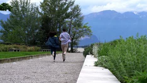 Back-View-Of-Romantic-Couple-Holding-Hands-While-Running-In-Laveno-Mombello,-Varese,-Italy