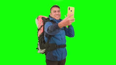 Ein-Mann-Mit-Wanderrucksack-Und-Gelbem-Smartphone-In-Einem-Studio-Mit-Greenscreen,-Der-Reiseinhalte-Für-Ein-Vblog-Erstellt