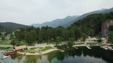 Toma-Aérea-Con-Dron-Cerca-Del-Lago-Bohinj-Sobre-Un-Estacionamiento-Y-Algunos-Muelles-En-Eslovenia-Con-Montañas-De-Fondo