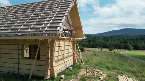 Casa-De-Madera-En-Construcción,-Hecha-De-Troncos-Y-Ubicada-En-Un-Hermoso-Paisaje-Durante-Un-Hermoso-Día-De-Verano,-Rodeada-De-Montañas,-Exuberante-Vegetación-Y-Césped.