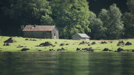 Tilt-shift-video-of-two-old-wooden-barns-on-the-rocky-coast-of-a-fjord,-with-the-unique-effect-adding-a-delightful,-model-like-appearance