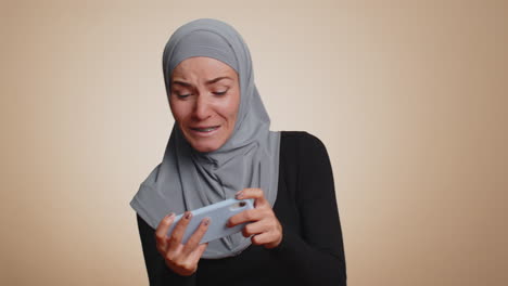 Worried-funny-addicted-muslim-girl-enthusiastically-playing-drive-racing-video-game-on-mobile-phone