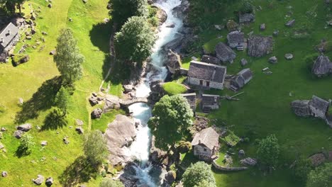 Aerial-view-of-a-scenic-landscape-with-a-river-flowing-through-a-valley-near-a-village-of-traditionally-built-houses-in-Maggiatal-Vallemaggia,-Tessin,-Switzerland