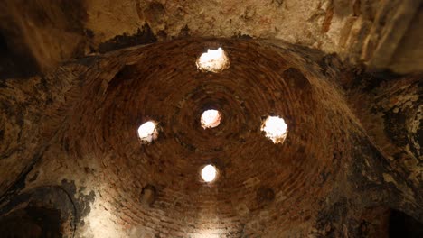 Interior-De-Una-Estructura-Antigua-Con-Columnas-De-Ladrillo,-Techos-Abovedados-Y-Un-Ambiente-Parcialmente-Iluminado,-Que-Resalta-La-Mezcla-De-Arquitectura-E-Historia.