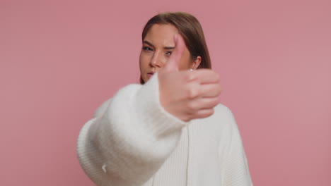 Upset-woman-in-white-sweater-showing-thumbs-down-sign-gesture,-disapproval,-dissatisfied-dislike