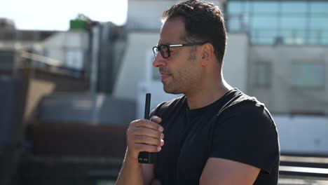 Security-guard-is-standing-on-a-rooftop-using-a-walkie-talkie-to-communicate-with-his-team