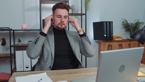 Businessman-working-on-laptop-at-office-wearing-earphones-listening-favorite-energetic-disco-music