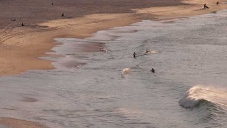 People-paddling-in-the-shallow-water-at-sunrise,-Bondi-Beach